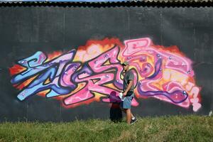 Young caucasian male graffiti artist drawing big street art painting in blue and pink tones photo