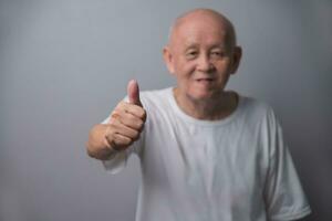 Asian bald senior man showing thumb up in white shirt photo