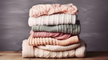 Bunch of knitted warm pastel color sweaters with different knitting patterns folded in stack on brown wooden table, grunged texture wall background. Fall winter season knitwear. Generative AI photo