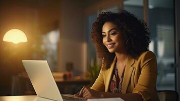 Smiling African American businesswoman sitting at table in her home office, reading documents and working using laptop photo