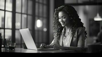 Smiling African American businesswoman sitting at table in her home office, reading documents and working using laptop photo