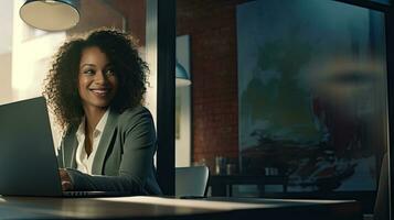 Smiling African American businesswoman sitting at table in her home office, reading documents and working using laptop photo