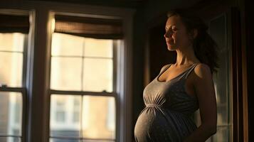 A pregnant woman stood smiling in the corner of the window with light streaming through the window. photo