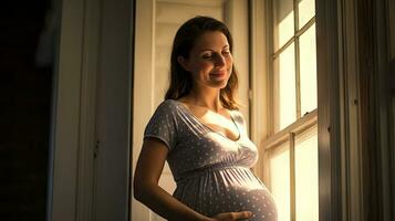 A pregnant woman stood smiling in the corner of the window with light streaming through the window. photo