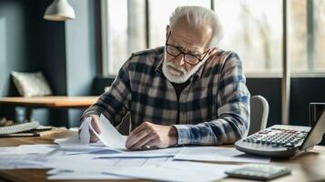 Elderly man sitting thinking, using laptop and writing in notebook at home table. Studying the concept of formula photo