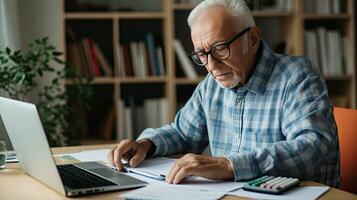 Elderly man sitting thinking, using laptop and writing in notebook at home table. Studying the concept of formula photo