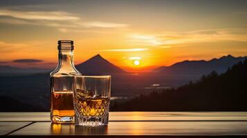 A whiskey glass and a bottle on a bar table In the background are mountains and a sea of mist at sunset. photo