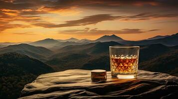 A whiskey glass and a bottle on a bar table In the background are mountains and a sea of mist at sunset. photo