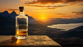 A whiskey glass and a bottle on a bar table In the background are mountains and a sea of mist at sunset. photo