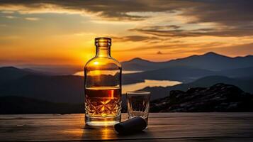 A whiskey glass and a bottle on a bar table In the background are mountains and a sea of mist at sunset. photo