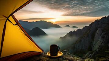 Camping holding a cup in an open yellow tent with a misty mountain lit by natural light. photo