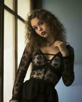 a beautiful young woman in a black lace bodysuit leaning against a window generative ai photo