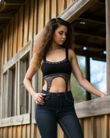 a woman in jeans and a crop top leaning against a wooden fence generative ai photo