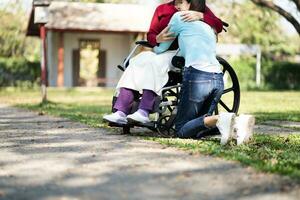 asiático mayor mujer en silla de ruedas con contento hija. familia relación retirado mujer sentado en silla de ruedas en el parque años cuidado a Jubilación hogar. foto