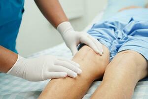 Doctor checking Asian elderly woman patient with scar knee replacement surgery in hospital. photo