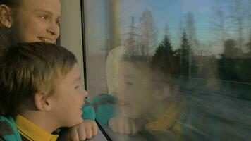 Small boy with mother sitting against window in their rail train place and watching outside video