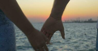cerca arriba Disparo de romántico Pareja participación manos en el playa en contra puesta de sol el pireo, Grecia video