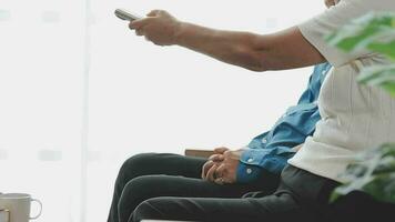 Happy senior couple using remote control to change channel. Seniors watch TV for entertainment while man using remote control. Wife and old man sitting on couch in living room with television show. video