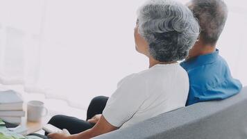 Happy senior couple using remote control to change channel. Seniors watch TV for entertainment while man using remote control. Wife and old man sitting on couch in living room with television show. video