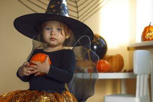 retrato de un pequeño niña en un bruja disfraz con un calabaza en su manos. foto
