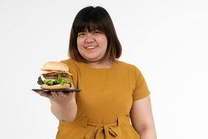 Hungry overweight young Asian woman holding hamburger on isolated background, Her hungry all time and overeat, gluttony and binge eating. Her lifestyle is eating fast food all time. Unhealthy Concept photo