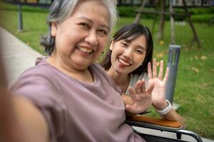 Happy Asian patients in a wheelchair use smartphones to take pictures with careful caregivers or nurse Concept of happy retirement with care from a caregiver and Savings and senior health insurance. photo