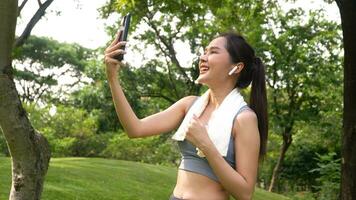 Asian woman attractive use smartphone for video conference with her friend after workout. Smiling sporty young woman working out outdoors and looking at camera. Healthy lifestyle well being wellness photo