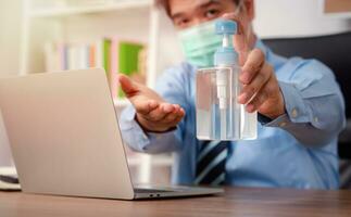 Businessman wearing a mask and use hand sanitizer on his desk for prevention or antibacterial hygiene and Coronavirus disease at the office. photo