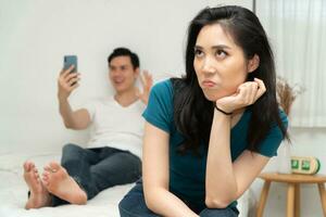 Unhappy Asian woman in bed and feeling Bored and grumpy her husband because tired of her husband who ignores her and uses the smartphone all time. Concept of relationship problem from technology photo