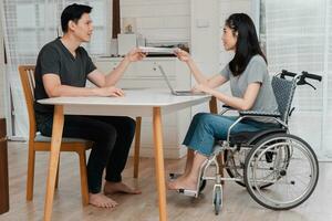 A woman in a wheelchair after a car accident and working with a computer at home with her lover. The concept of Mutual care and new technology has made people with disabilities Equality in society. photo