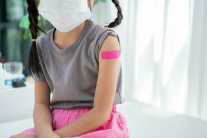 Close-up of medicinal plaster after vaccinated in shoulder of Asian girl kids in hospital. Pediatrician makes vaccination for kids. Vaccination, immunization, disease prevention concept. photo