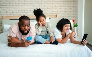 African American girls are not satisfied and sad, sitting in the middle between father and mother. Parents Are using the smartphone and abandoned children. Children need their parents attention. photo