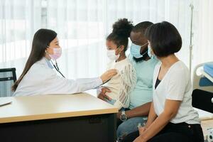 Asian woman pediatrician doctor hold stethoscope for exam a little girl patient and heck heart lungs of kid, Good family doctor visiting child at home, Healthcare and medicine for childhood concept. photo