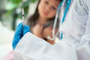 Doctor holding syringe for prepare vaccinated in the shoulder of Asian girl kids in the hospital. Pediatrician makes vaccination for kids. Vaccination, immunization, disease prevention concept. photo