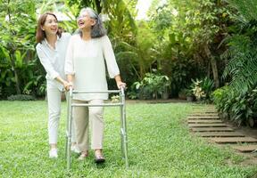 An old elderly Asian woman uses a walker and walking in the backyard with her daughter.  Concept of happy retirement With care from a caregiver and Savings and senior health insurance photo