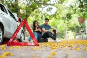 Asian couple using smartphone for assistance after a car breakdown on street. Concept of vehicle engine problem or accident and emergency help from Professional mechanic photo
