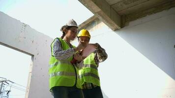 Aziatische ingenieur of jonge vrouwelijke architect zet een helm op voor veiligheid en praat met een aannemer over een bouwproject voor een fabrieksgebouw, concept van teamwork, leiderschapsconcept. video