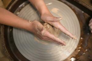 Potter girl works on potter's wheel, making ceramic pot out of clay in pottery workshop photo