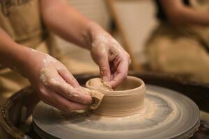 Potter girl works on potter's wheel, making ceramic pot out of clay in pottery workshop photo