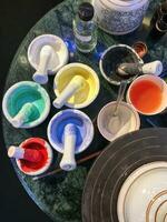 Cups and bowls used as color pots plus well worn brushes standing on a rock table used to paint pottery. photo