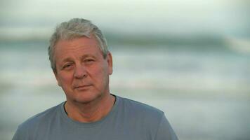 Senior man with a slight smile, portrait against the sea video