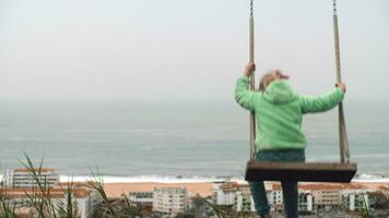 Little girl on swing overlooking Nazare ocean coast with hotels, Portugal video