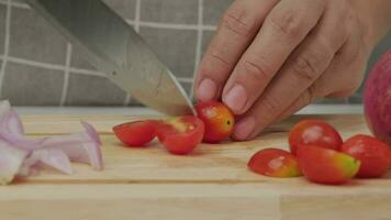 kvinna hand använder sig av kök kniv till skära mogen tomat på trä- skärande styrelse. kvinna är framställning mat i kök på Hem. matlagning begrepp. video