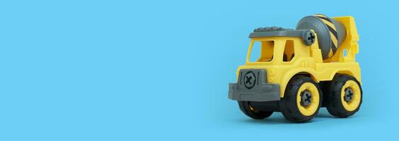 Yellow plastic concrete mixer truck toy isolated on blue background with copy space for banner of toy store. photo