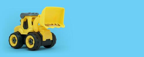 yellow plastic bulldozer toy isolated on blue background with copy space for toy store banner photo