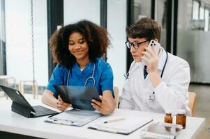 Doctor Talks With Professional Head Nurse or Surgeon, They Use Digital tablet Computer. Diverse Team of Health Care Specialists Discussing Test Result on desk in hospital photo