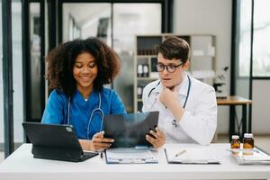 Doctor Talks With Professional Head Nurse or Surgeon, They Use Digital tablet Computer. Diverse Team of Health Care Specialists Discussing Test Result on desk in hospital photo