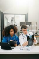 Doctor Talks With Professional Head Nurse or Surgeon, They Use Digital tablet Computer. Diverse Team of Health Care Specialists Discussing Test Result on desk in hospital photo