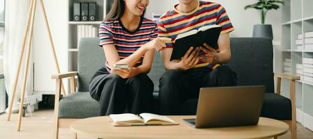 Two asian students learning together online with a laptop, tablet and tutor together in living room photo