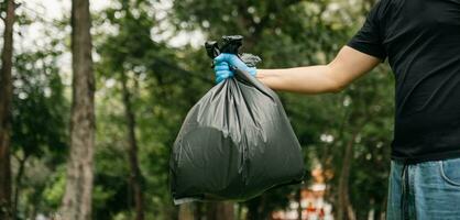 Hand holding garbage black bag putting in to trash to clean. Clearing, pollution, and plastic concept. photo